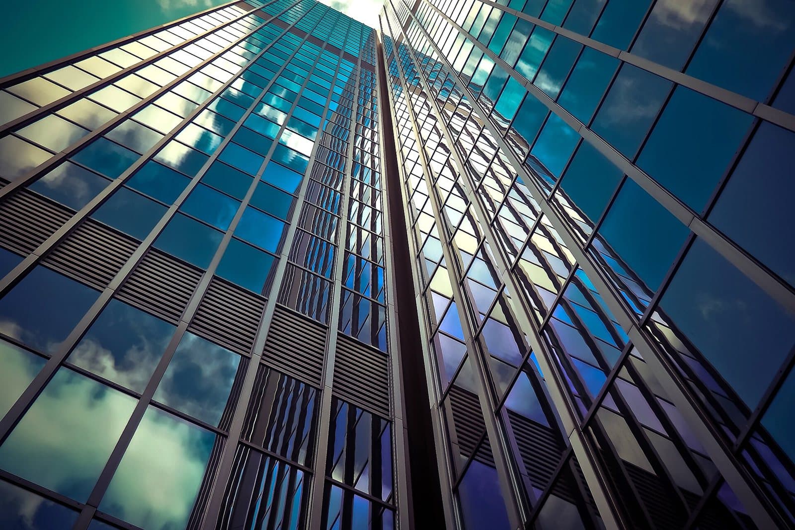 Looking up between glass-clad towers, their facades reflecting each other and the sky.