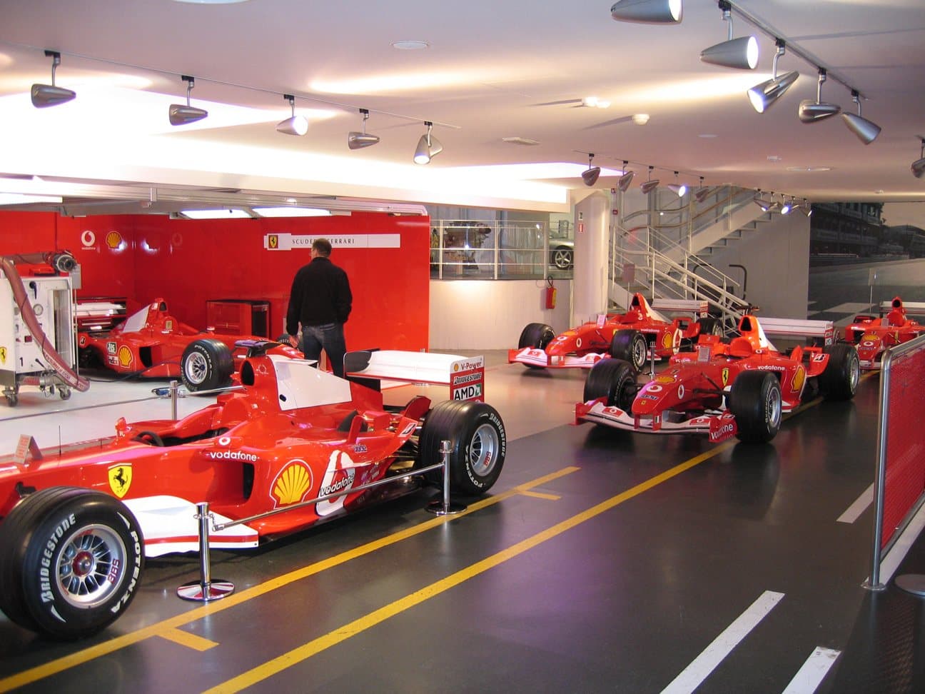 A row of red Formula One cars lined up nose to tail in a museum hall.