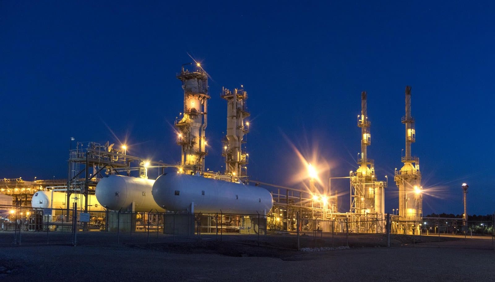 A refinery lit up at dusk, its distillation columns and pipework picked out by thousands of lights.