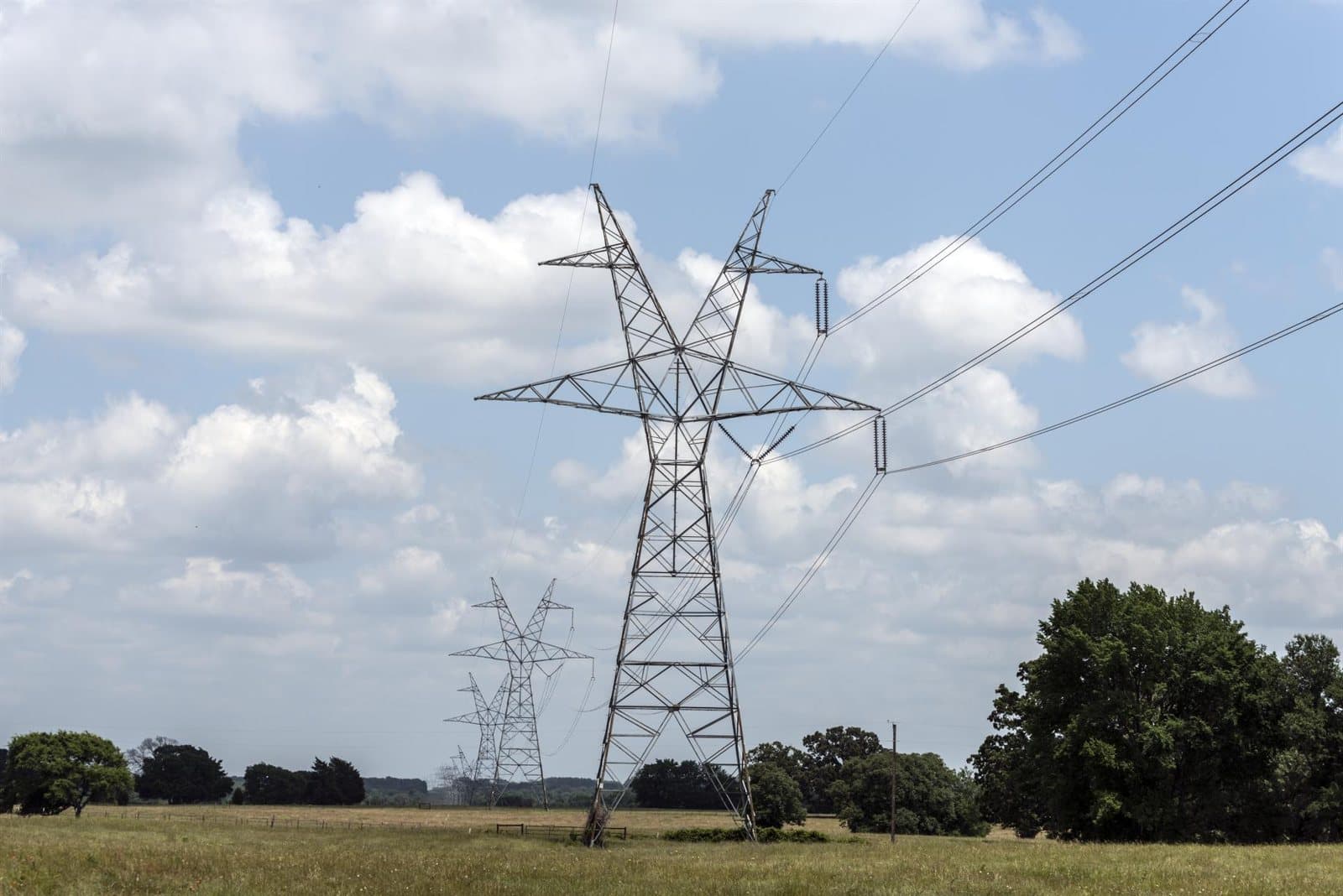 A line of lattice transmission towers marching away across open country, carrying conductors toward the horizon.
