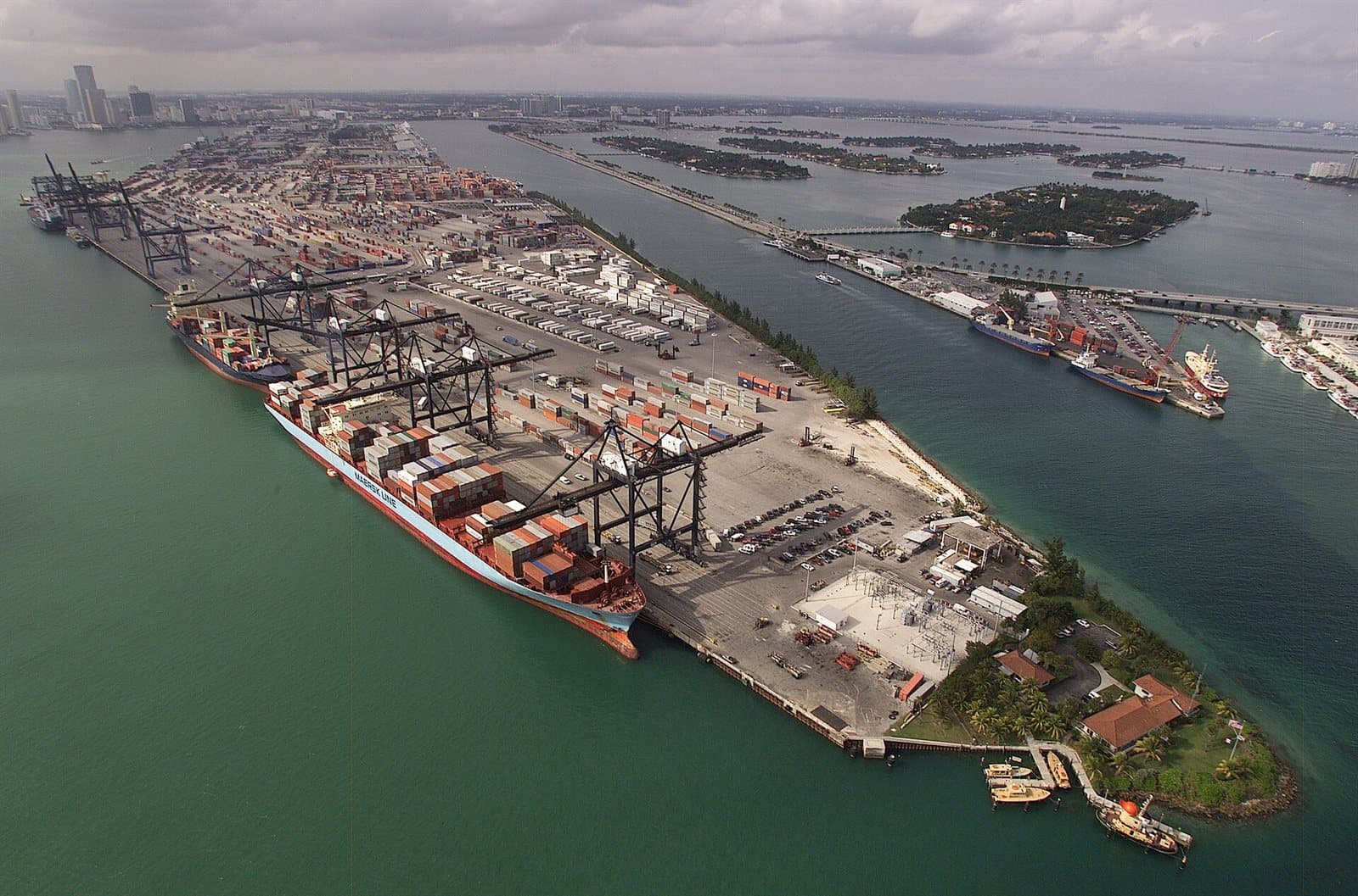 An aerial view of a container terminal, stacked containers and gantry cranes laid out in blocks along the waterfront.