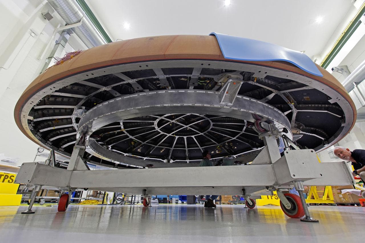 A large circular spacecraft heat shield seen face on, its dark surface divided into a honeycomb of blocks.
