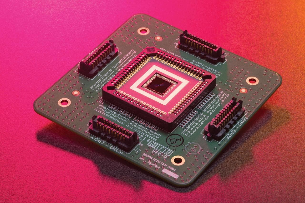 A close view of a detector chip at the centre of a circuit board, its square die framed by gold contacts.