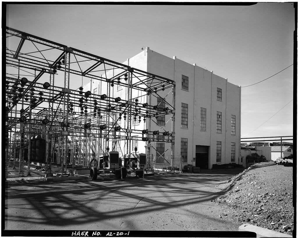 Exterior of the Crosscut Steam Plant, its tall window bays rising behind the steel framing and insulators of the switchyard.
